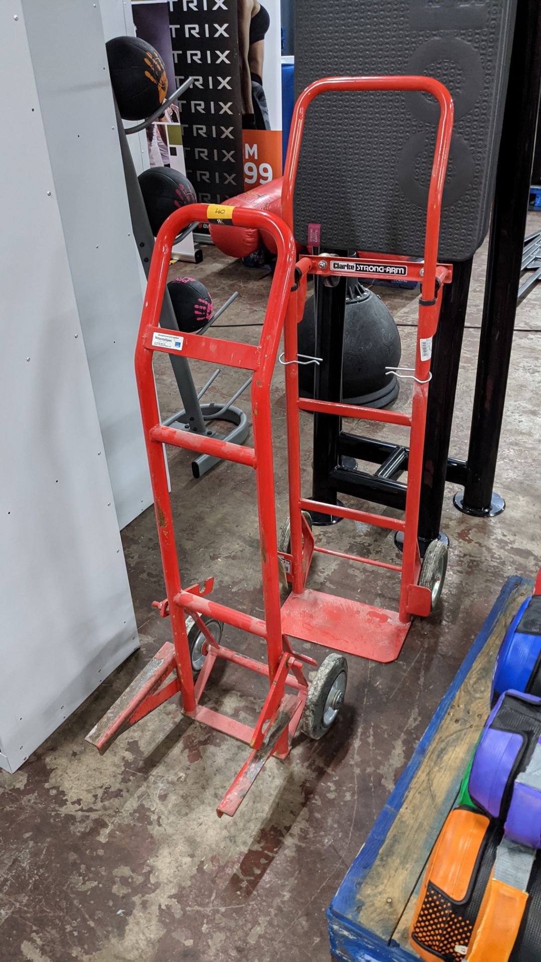 2 off red metal sack trucks, one with conventional foot plate & the other as pictured