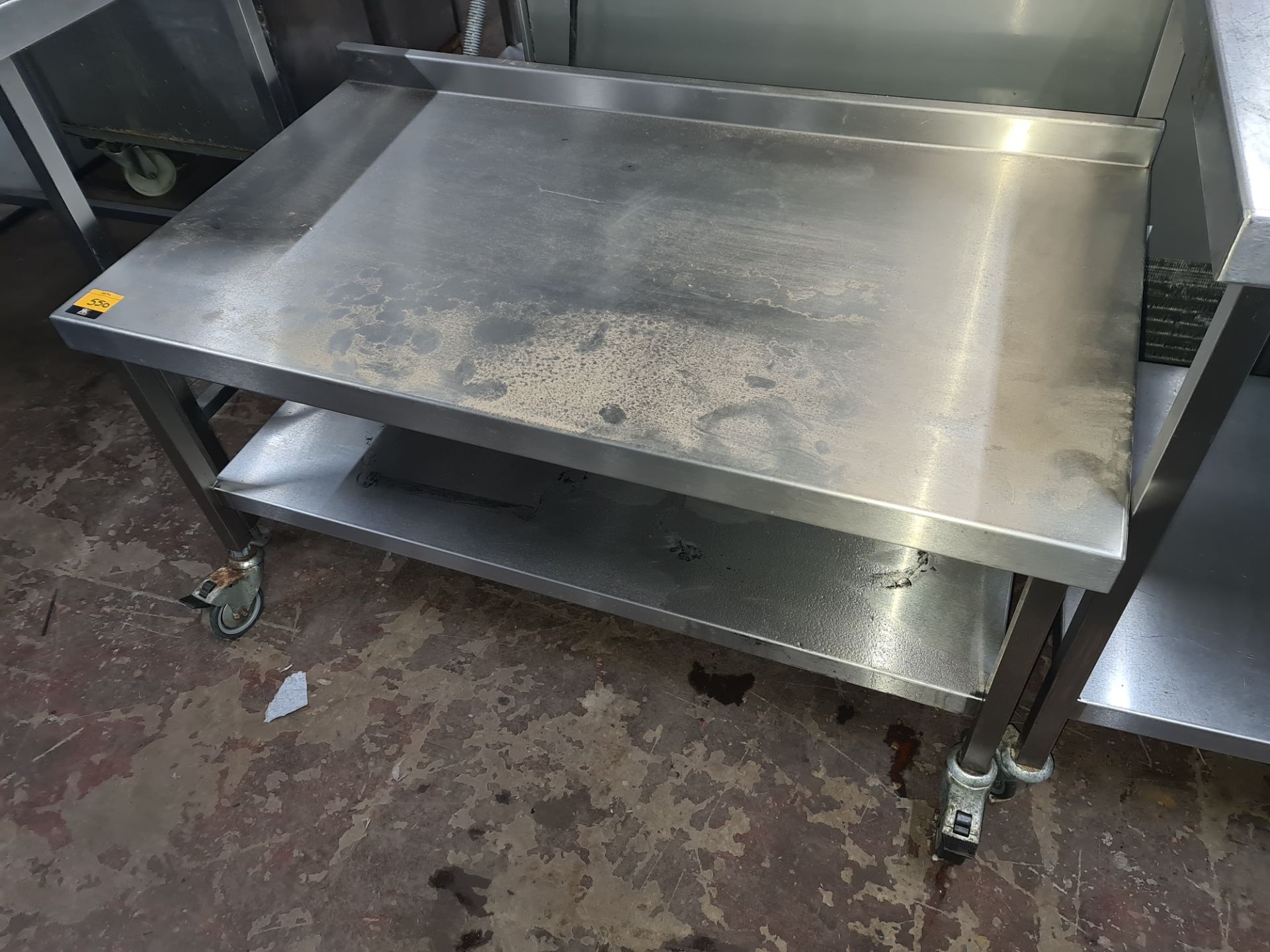 Stainless steel twin-tier table with splashback measuring 1200mm x 670mm x 600mm