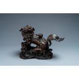 A Chinese bronze model of a Buddhist lion on a finely carved wooden stand, 18th C.