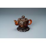 A Chinese carved amber teapot and cover on wooden 'lotus' stand, 19th C.