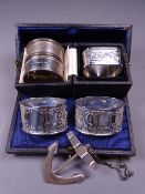 CASED & OTHER NAPKIN RINGS (5) with a hallmarked port decanter label in the shape of an anchor,