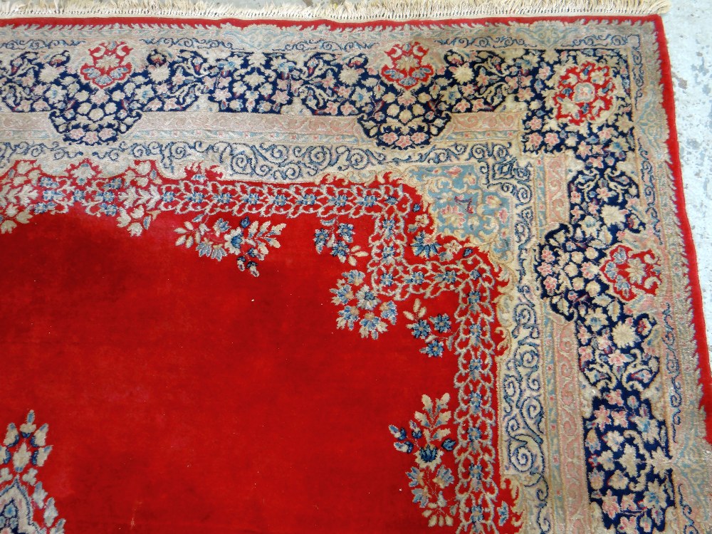 KIRMAN CARPET, indigo and ivory rectangular medallion with pendants on a plain cherry red field with - Image 7 of 11