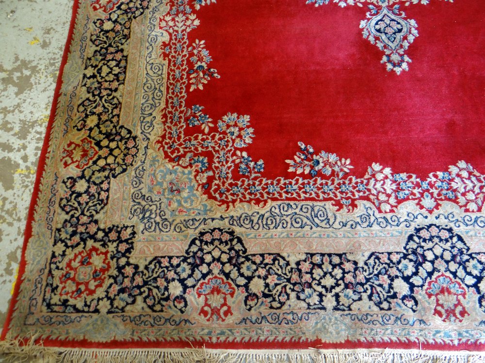 KIRMAN CARPET, indigo and ivory rectangular medallion with pendants on a plain cherry red field with - Image 3 of 11