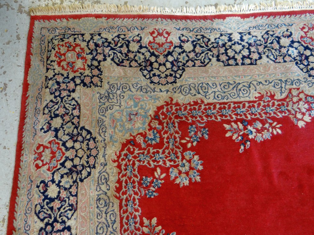 KIRMAN CARPET, indigo and ivory rectangular medallion with pendants on a plain cherry red field with - Image 8 of 11