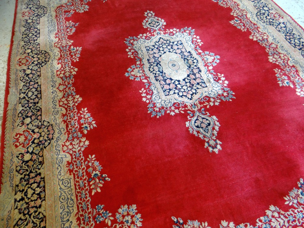 KIRMAN CARPET, indigo and ivory rectangular medallion with pendants on a plain cherry red field with - Image 4 of 11