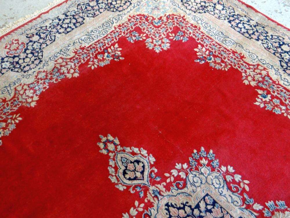 KIRMAN CARPET, indigo and ivory rectangular medallion with pendants on a plain cherry red field with - Image 9 of 11