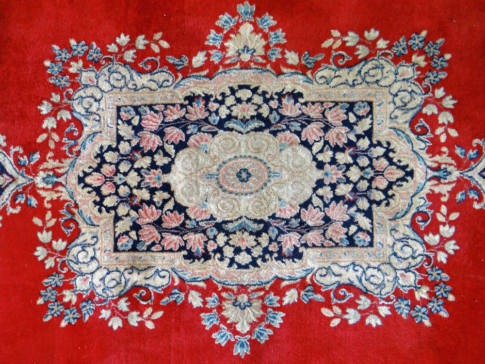 KIRMAN CARPET, indigo and ivory rectangular medallion with pendants on a plain cherry red field with - Image 11 of 11