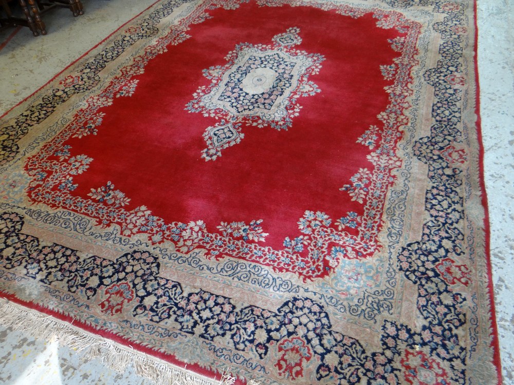 KIRMAN CARPET, indigo and ivory rectangular medallion with pendants on a plain cherry red field with - Image 2 of 11