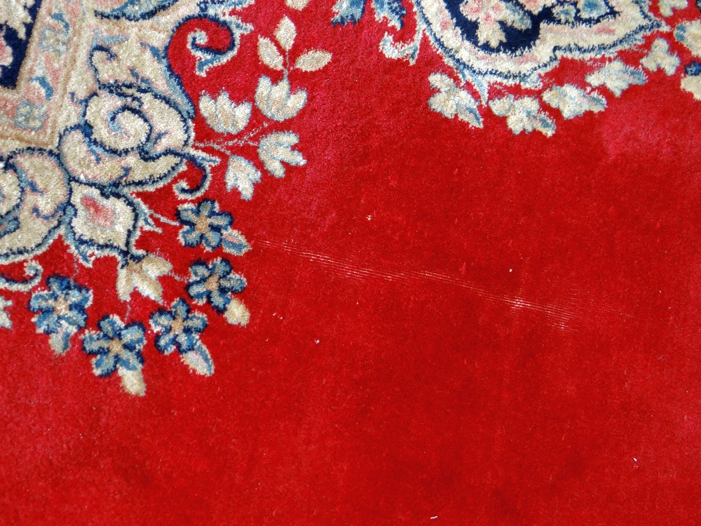KIRMAN CARPET, indigo and ivory rectangular medallion with pendants on a plain cherry red field with - Image 6 of 11
