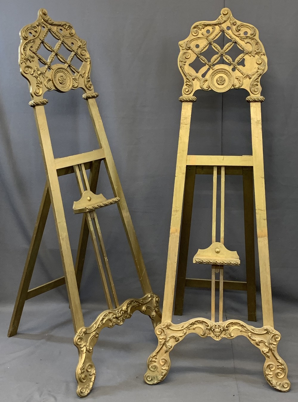 TWO LARGE VINTAGE GILT DECORATED EASEL STANDS having lattice work and applied mouldings with
