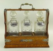 20TH CENTURY OAK THREE BOTTLE TANTALUS, the cut glass spirit decanters each with silver decanter