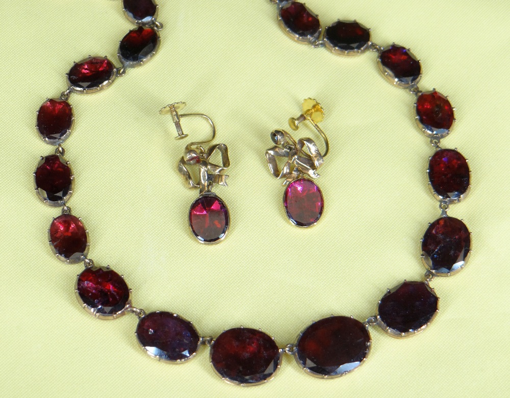 GARNET SET RIVIERE NECKLACE, the thirty graduated oval-shaped stones closed set in yellow metal,