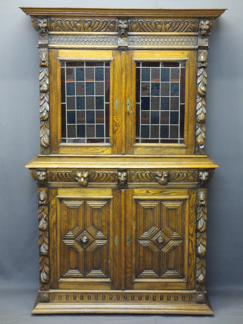 CONTINENTAL STYLE CARVED OAK BOOKCASE SIDEBOARD - with leaded coloured glass upper doors, lion mask,