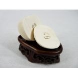 AN IVORY APPLE IN TWO HALVES - showing the pips on a small carved wooden hardwood fretwork stand,