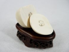 AN IVORY APPLE IN TWO HALVES - showing the pips on a small carved wooden hardwood fretwork stand,