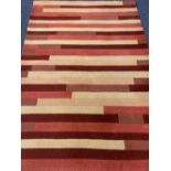 MODERN HAND LOOMED INDIAN WOOL PILE RUG having tonal reds and creams in a repeating block pattern,