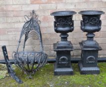 PAIR CAST IRON GARDEN URNS ON PLINTHS, decorated with scrolling foliage on laurel wreath