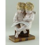 CONTINENTAL FAIENCE FIGURAL GROUP of two putti singing from a song sheet whilst seated on bookstack