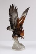 Porzellanfigur. Einfliegender Steinadler auf Felssockel. Naturalistische Bemalung in Grau-und