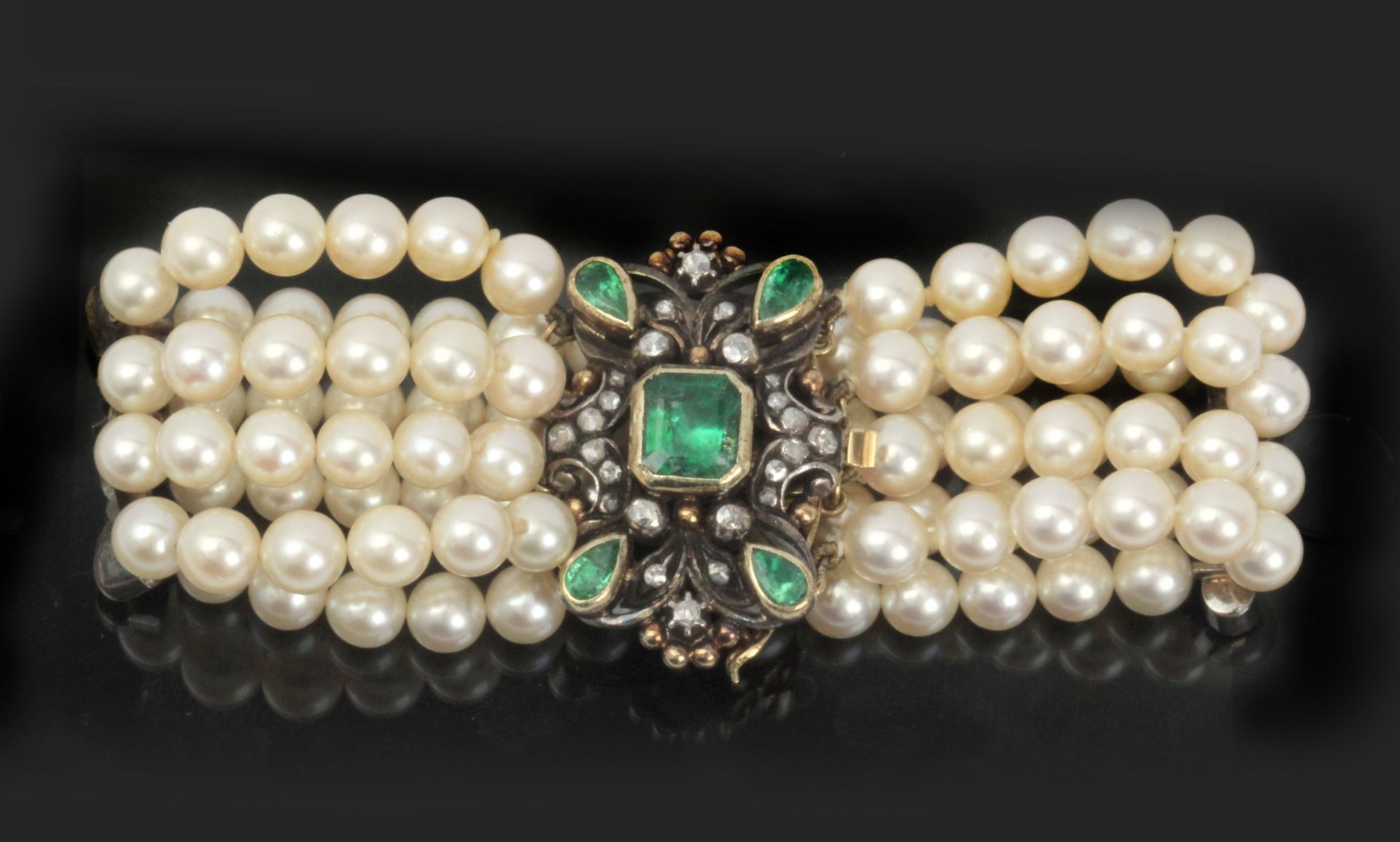 A four strand cultured pearl bracelet with a silver and gold clasp mounted with emeralds
