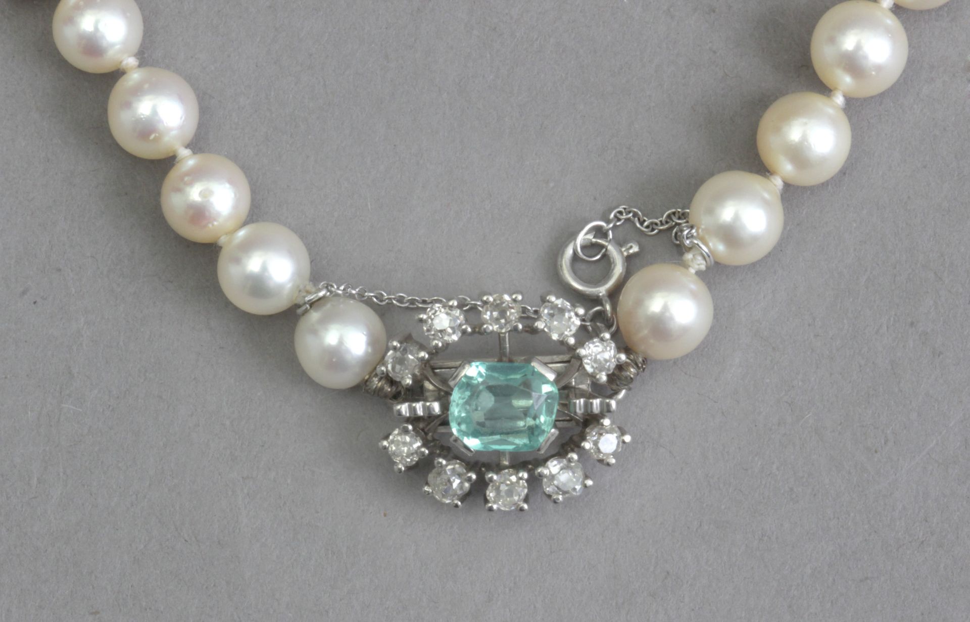 A cultured pearl necklace with an emerald and diamond brooch clasp