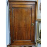 An Oak hanging Corner Cupboard enclosed by a rectangular molded paneled door with exposed H shaped