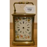 A brass carriage timepiece, with floral decorated white dial, hands and key.