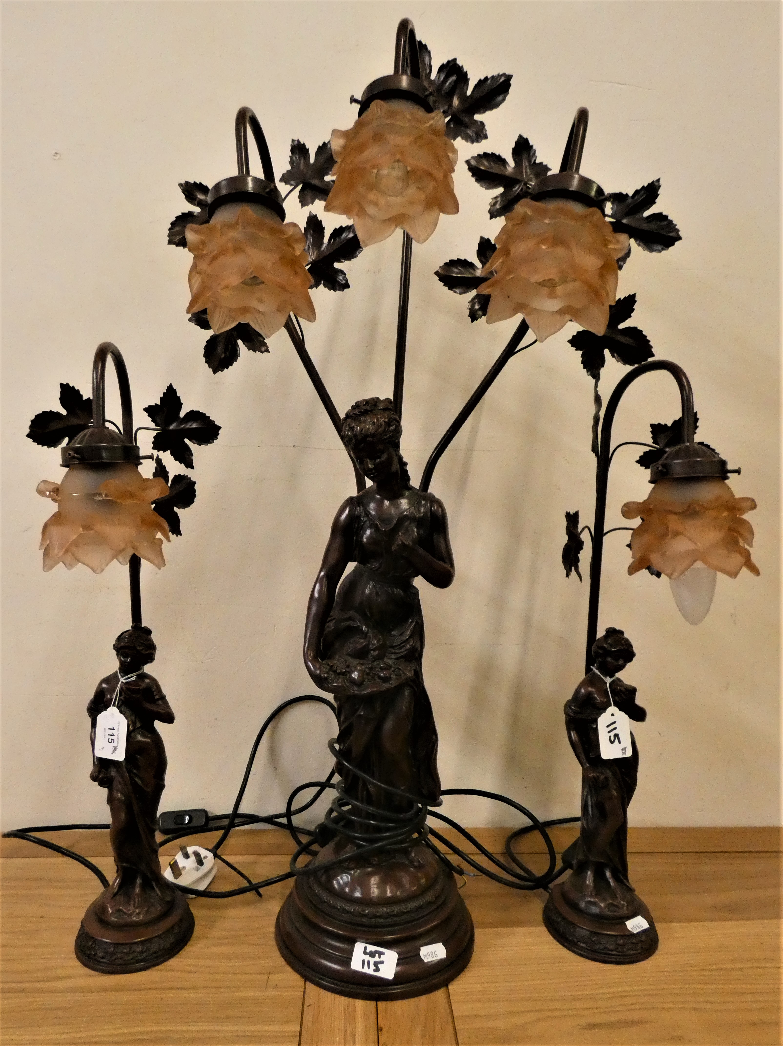 A bronze effect table lamp garniture, in the form of a lady holding a basket, triple pale pink