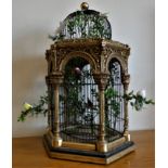 An ornate gilt hexagonal birdcage with domed wire top, the arches side panels of classical style