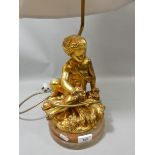A table lamp in the form of a gilt cherub seated on a marble base with beige shade. 65cm tall.