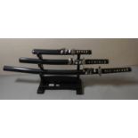 Three decorative samurai swords on stand.