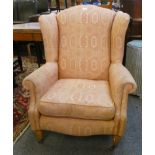 A pink upholstered wingback armchair, raised on tapering legs with brass castors and a stained beech