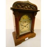 An oak cased manual wind mantle clock with arched and carved pediment. 38cm tall.