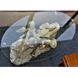 An oval glass topped occasional table approx 115cm long on a moulded cherub base