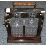A Tantalus with oak frame and metal fittings, including two cut glass decanters (one AF)