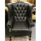 A black leather button back wing armchair