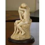 A resin sculpture of a couple embracing on wooden plinth.