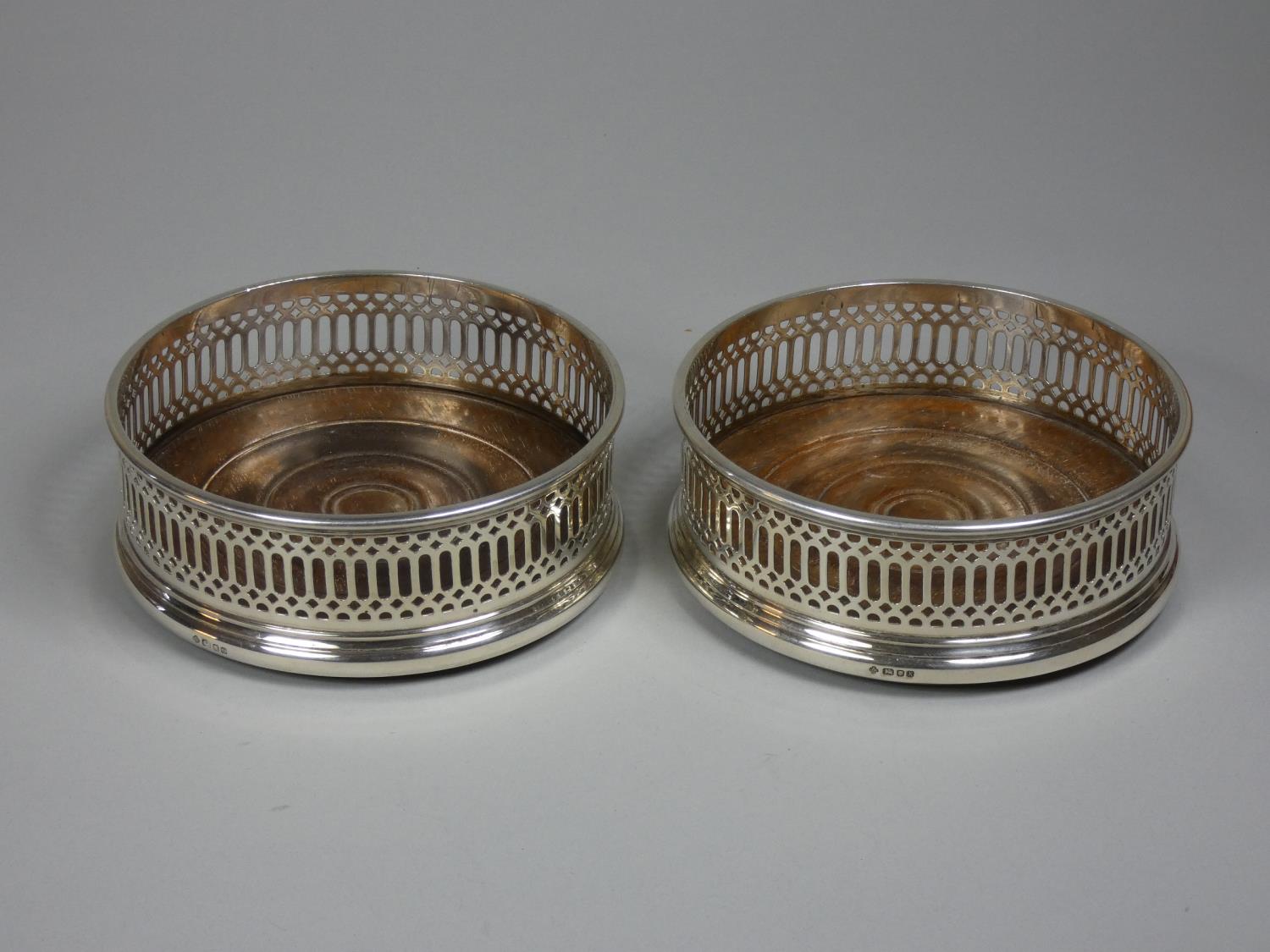 A pair of silver bottle coasters, London 1984, with pierced border and turned mahogany base,
