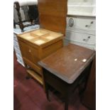 A teak sewing cabinet on casters with hinged top and storage compartment with draws at either side