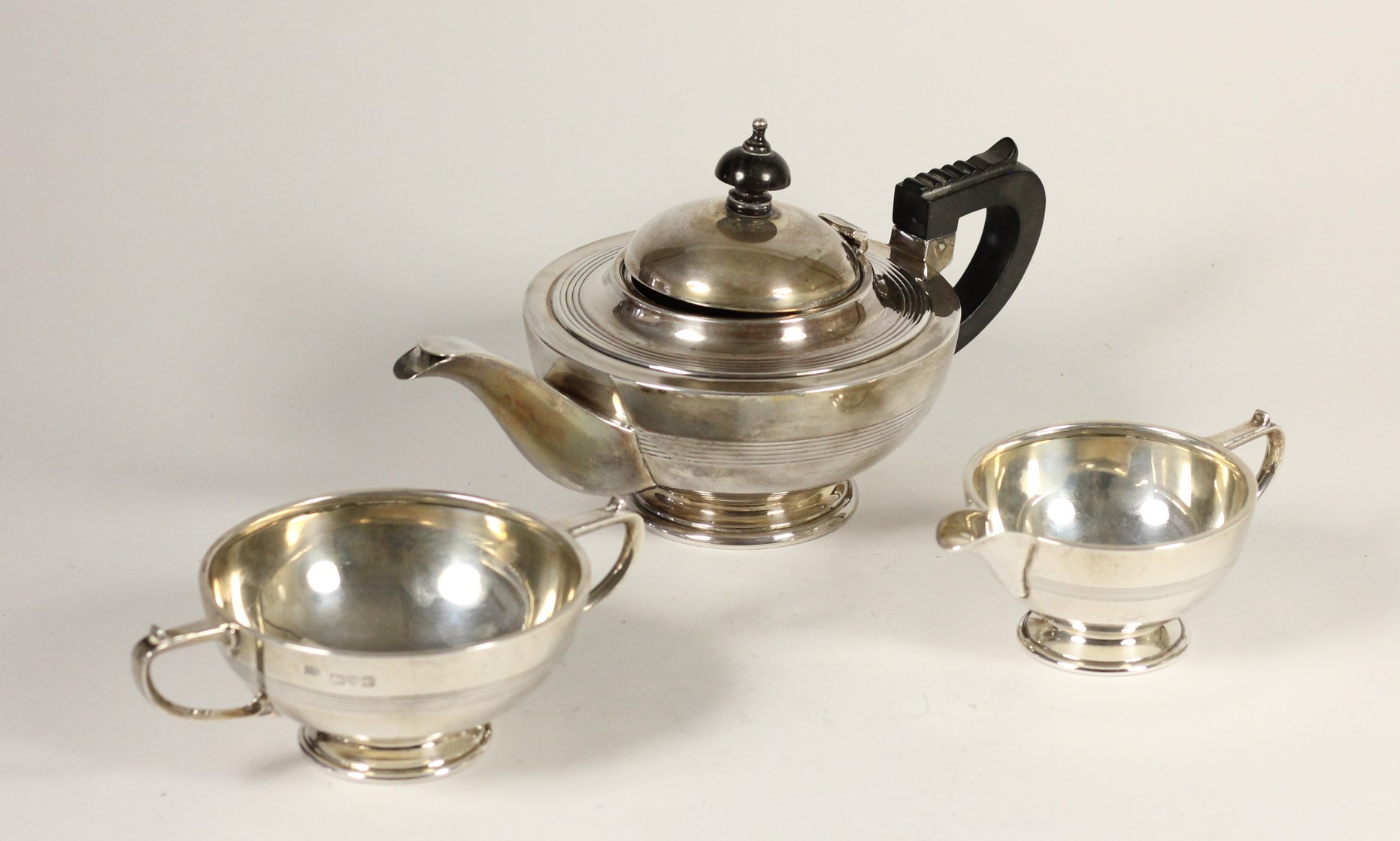 A silver three piece bachelor tea service, by Barker Bros, Chester 1919/21, of circular form with