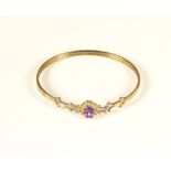 A 9ct gold Victorian style sprung bangle, the scroll front set with a mixed cut amethyst, 6.2gm