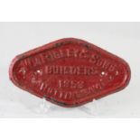 A red triangualr cast-iron wagon plate, 'W.M Rigley & Son Builders Nottingham 1953'