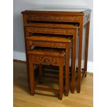 A Chinese nest of four hardwood tables, carved with Oriental scenes, glazed top, 67cm (Height of