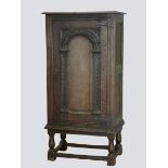 A 19th century oak food cupboard on stand with carved arch door, wrought iron hinges, the sides with
