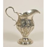 An Edwardian silver cream jug, Birmingham 1905, in the George II style with embossed decoration,