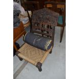 An ethnic style low recliner chair having carved frame, strung seat and additional jewelled style