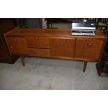 A vintage teak long john style sideboard, with brass drop handles, label removed from drawer (coin