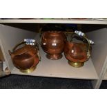 Three copper and brass coal helmets, two having patterned ceramic handles and the other wooden