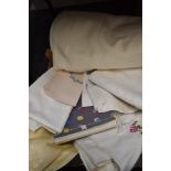 A box full of vintage and retro table linen including damask and some embroidered items.