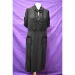 A 1940s black crepe dress with frilled details,bow to neckline and tucks to skirt, around a medium